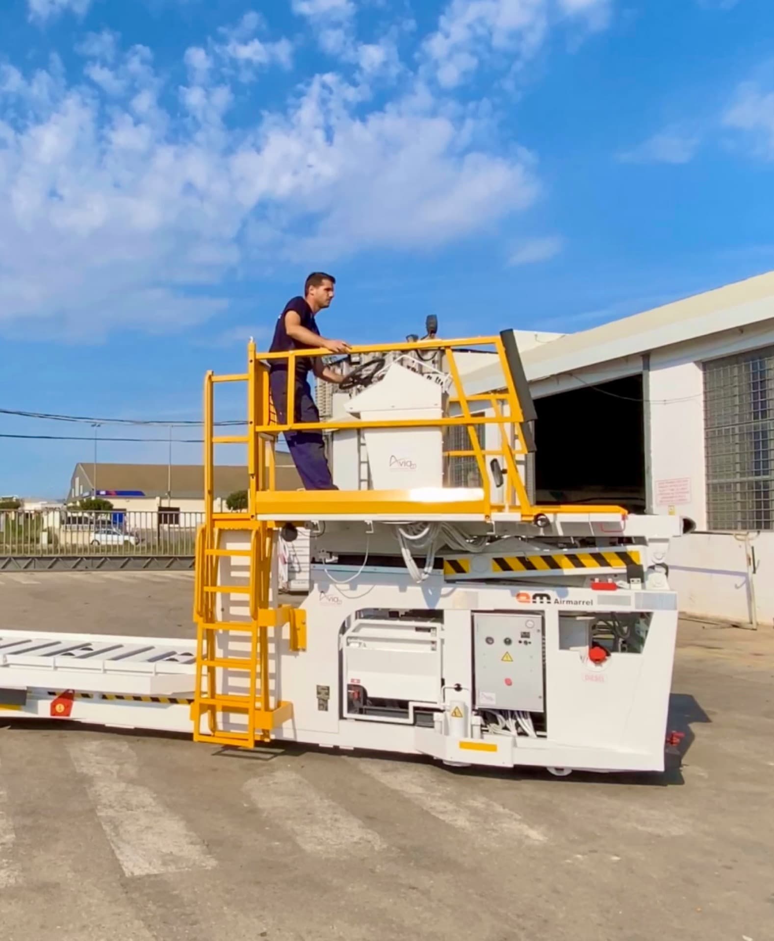 White ground support vehicles parked outside the Aviaco GSE workshop, a belt loader and a service truck under the branded hangar sign.