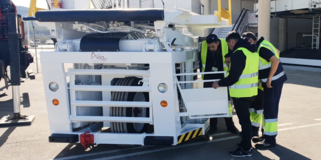Group of workers in high-visibility vests inspecting a large white industrial machine outdoors with panels open and wheels visible.