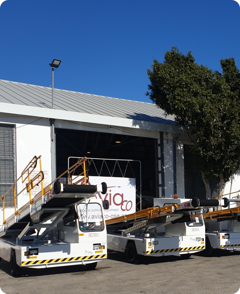 Multiple white Aviaco belt loader vehicles parked outside hangar